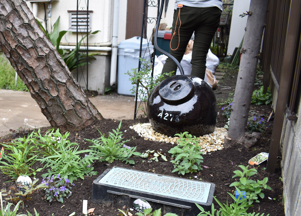 東京都世田谷区の「ふくふくのいえ」は、空き家を活用して、子育て支援サロン「おでかけひろばFUKU＊fuku」の集いの場になっている。こちらは雨水を活用した宿根草ガーデン。奥の丸いかめが雨水タンクで、アーチにつながっているホースは雨どいにつながっている。