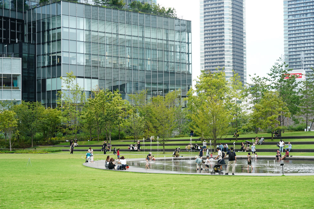 うめきた公園（南公園）。水盤で遊ぶ子どもたちや、アンフィローンに座って食事をする人たちが見られる。
